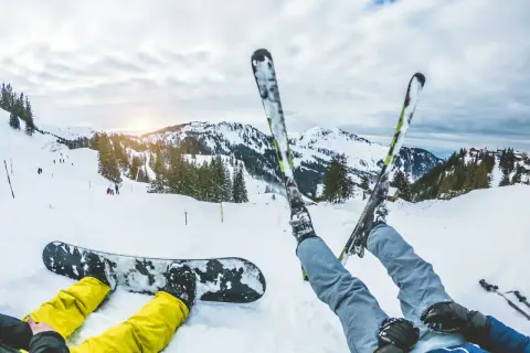 Narciarz i snowboardzista odpoczywają na stoku. Zastanawiasz się, co bardziej obciąża kolana: narty czy snowboard? Góry i słońce zachęcają do jazdy.