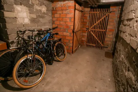 Wspólna piwnica w bloku, gdzie stoją rowery. W tle drewniane drzwi i ceglane ściany.