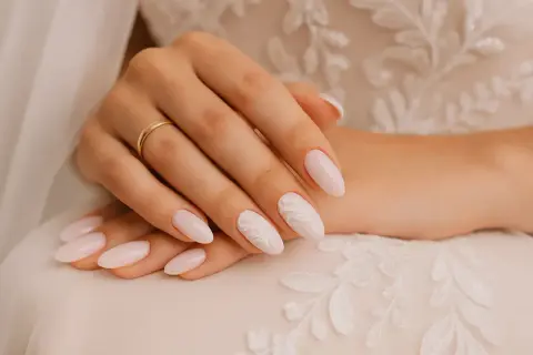 Mains d'une mariée aux ongles pastel ornés de dentelle blanche, parfaits pour un mariage.