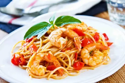 Spaghetti con gamberetti succulenti e pomodorini freschi, guarniti con basilico. Un piatto invitante che profuma di mare.