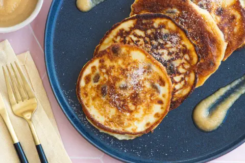 Goldene quarkkeulchen ohne kartoffeln, bestreut mit Zucker, serviert mit Apfelmus auf einem dunklen Teller.