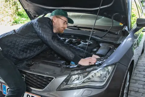 Man med keps och glasögon böjer sig över motorhuven för att byta halogenlampa.