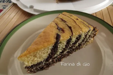Una fetta di torta zebrata, con strati alternati di impasto chiaro e scuro, su un piatto con bordo verde.