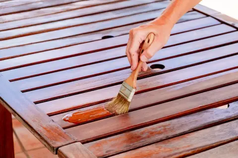Mano aplicando barniz a una mesa de madera. Se puede barnizar sin tapaporos para un acabado rápido y protector.