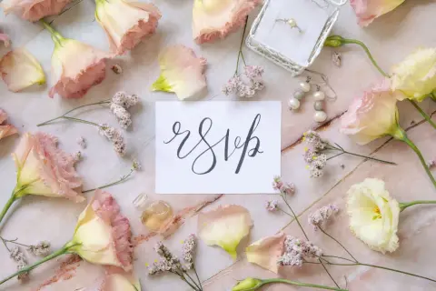 Delikatne kwiaty, pierścionek i kolczyki otaczają kartkę z napisem "rsvp". Czy wiesz, rsvp co to znaczy?