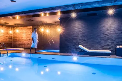 Mężczyzna w szlafroku spaceruje po luksusowej strefie dla dorosłych z basenem i jacuzzi.