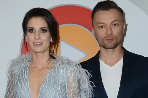 Sylwia Grzeszczak i Liber pozują do zdjęcia. Ona w błyszczącej sukni z piórami, on w granatowej marynarce.