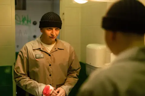 Chłopak w czapce i beżowej kurtce, z bandażem na ręce, patrzy w lustro. Scena z freestyle film.