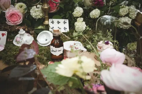 Décoration de mariage thème Alice au Pays des Merveilles : théière, cartes à jouer, et la fameuse bouteille "Drink me" sur un lit de mousse.