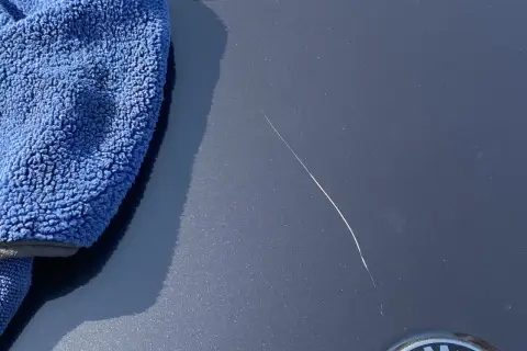 Un panno blu accanto a un graffio sulla vernice dell'auto, pronto per imparare come ritoccare vernice auto.