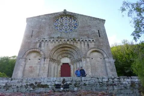 Dos personas posan frente a la fachada románica de Santo Estevo de Ribas de Miño, con su rosetón y portal detallados.