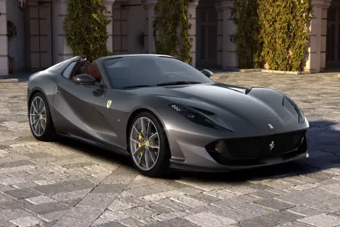 Szary kabriolet Ferrari 812 GTS z żółtymi zaciskami hamulcowymi stoi na brukowanym dziedzińcu przed budynkiem porośniętym bluszczem.