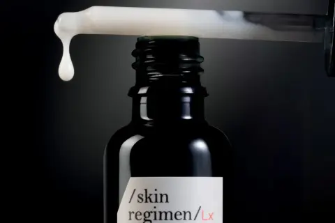 Una goccia di siero cade da un contagocce su una bottiglia scura, un passo essenziale nelle fasi skincare per una pelle radiosa.