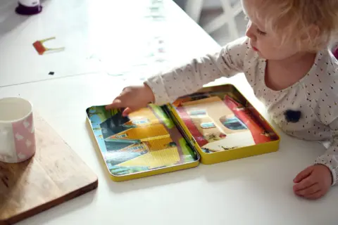 Małe dziecko bawi się otwartym pudełkiem z obrazkami domków, które są świetnymi zabawkami wspierającymi rozwój mowy.