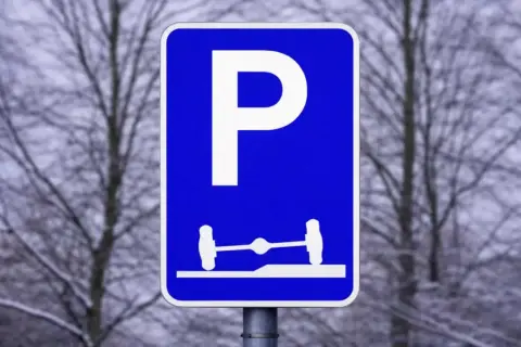 Blå parkeringsskylt med vitt P och en bild av en axel med hjul på en ramp. Förståelse av parkeringsskyltar är viktigt för att veta var man får parkera.