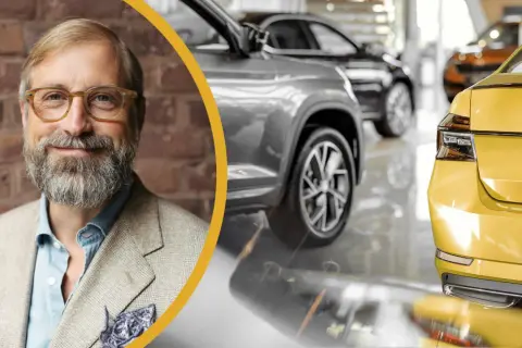 En leende man med glasögon och skägg står framför en rad bilar. Han är klädd i kavaj och ser ut att kunna serva bilen åt dig.