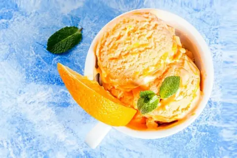 Erfrischendes orangen sorbet in einer Schale, garniert mit Minze und einer Orangenspalte auf blauem Untergrund.