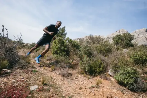 Un coureur en pleine action sur un sentier rocailleux, profitant d'une course à étapes dans un paysage aride et montagneux.