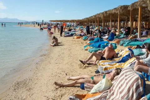 Ludzie odpoczywają na plaży w Egipcie. Idealna pogoda w Egipcie w grudniu sprzyja relaksowi na leżakach pod palmowymi zacienionymi wiatami.
