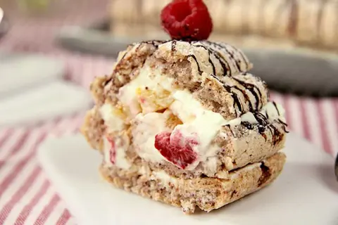 En läcker budapestbakelse med vispgrädde, frukt och chokladdrizzle, toppad med ett hallon.