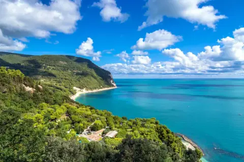 Vista mozzafiato dal belvedere Monte Conero: mare azzurro, costa verdeggiante e nuvole bianche nel cielo.