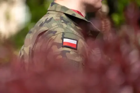 Żołnierz w mundurze z polską flagą. W tle zamazane czerwone liście i zieleń. Choroby dyskwalifikujące ze służby wojskowej mogą wpłynąć na możliwość noszenia takiego munduru.
