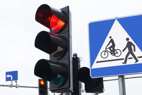 Sygnalizacja świetlna pokazuje czerwone światło, a obok znak informuje o przejściu dla pieszych i rowerzystów. Nie ryzykuj przejazdu na czerwonym świetle!