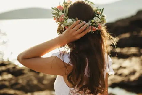 Frau mit Blumenkranz am Kopf, genießt die Sonne am Meer. Ein Bild von Mittsommer Ritualen.