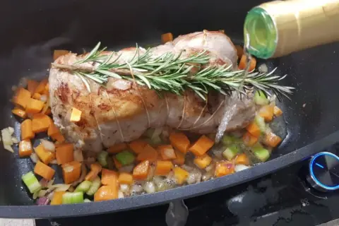 Arrosto di vitello in pentola con verdure e rosmarino, mentre viene sfumato con vino bianco.