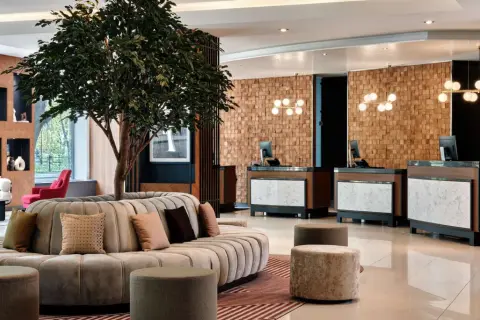 Eleganckie lobby hotelu Radisson Blu Hotel Krakow z okrągłą sofą, drzewem i recepcją z drewnianą ścianą.
