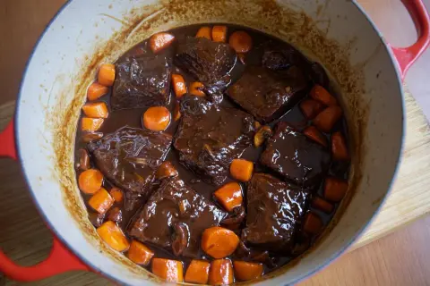 Sabroso plato típico de Francia: ternera estofada en salsa oscura con zanahorias y champiñones en una olla roja.