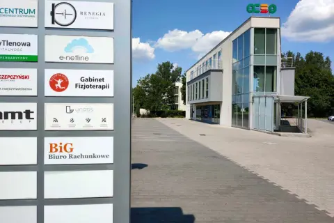 Tablica z nazwami firm, w tym "BiG Biuro Rachunkowe", przed nowoczesnym budynkiem biurowym.