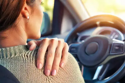 Femme au volant, main sur l'épaule, souffrant de tendinite. La conduite de voiture peut être douloureuse.