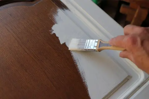 Une main applique une sous-couche claire sur un meuble en merisier, avant de le repeindre en noir.