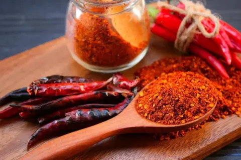 Ein Holzlöffel voller Cayennepfeffer-Flocken zeigt, woraus Cayennepfeffer hergestellt wird: getrocknete Chilischoten.
