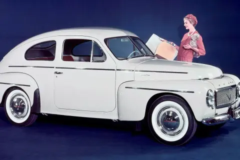 En vit Volvo PV 444 med en kvinna och en hund bredvid.