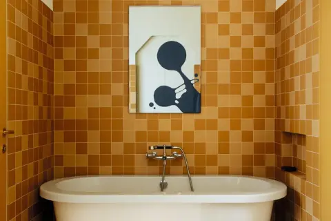 Salle de bain aux tendances carrelage ocre, baignoire blanche et miroir abstrait.