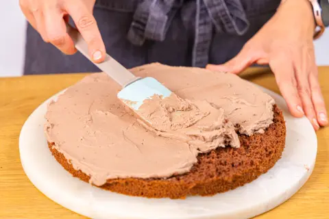 Eine Schokoladentorte wird mit einer cremigen Füllung bestrichen, die an Kinder Bueno Torte erinnert.