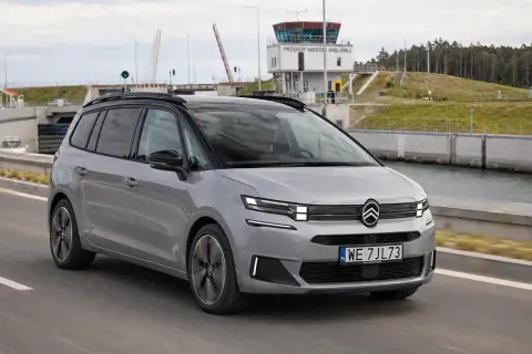 Srebrny Citroen Picasso jedzie drogą obok kanału. W tle widoczna wieża kontrolna i podniesiony most.