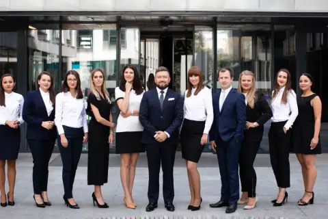 Grupa profesjonalistów w eleganckich strojach stoi przed nowoczesnym budynkiem.