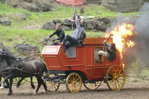Ein Wagen brennt bei einer Karl May Inszenierung in Elspe. Zwei Männer kämpfen, einer fällt aus dem brennenden Wagen.