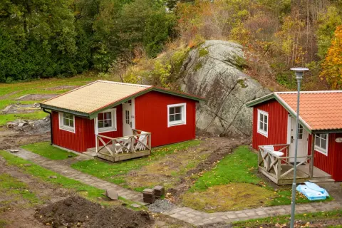 Dos casitas rojas de madera, ideales para un terreno. Rodeadas de naturaleza y una gran roca.