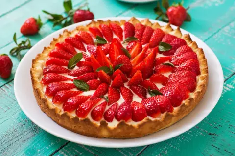 Pyszna tarta z owocami, pełna świeżych, czerwonych truskawek i listków mięty, na chrupiącym spodzie.