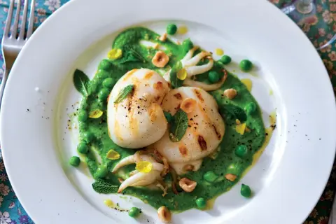Deliziosi seppie alla griglia su un letto di crema di piselli, guarnite con menta fresca e nocciole tostate.