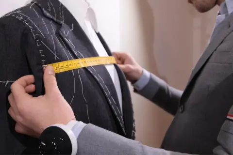 Sarto misura la giacca con metro giallo, prendendo nota della lunghezza braccio uomo per una vestibilità perfetta.