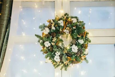 Corona de Adviento con piñas, algodón y canela, ideal para decorar una ventana de Navidad. Luces cálidas la iluminan.