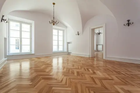 Un ampio salone con parquet a spina di pesce appena levigato, illuminato da grandi finestre e lampadari antichi.