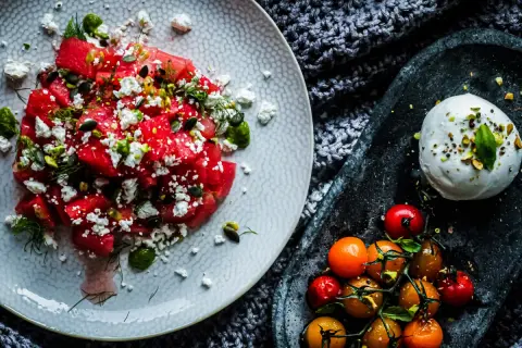 Salade de pastèque, feta, pistaches et tomates cerises, avec une burrata crémeuse. Un délice estival qui rappelle la tomate mozzarella.