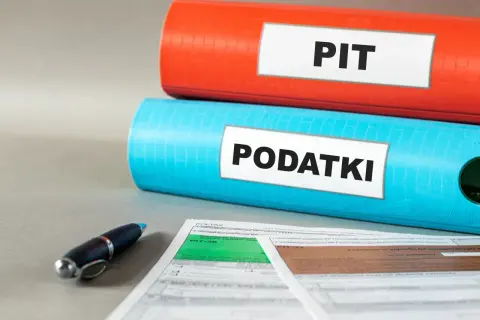 Dwa segregatory z napisami "PIT" i "PODATKI", obok formularze podatkowe i długopis. Kto nie płaci podatku do 26 roku życia?