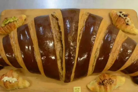 Un croissant gigante con glaseado de chocolate y pequeños croissants decorados, perfectos para un desayuno en Zaragoza.